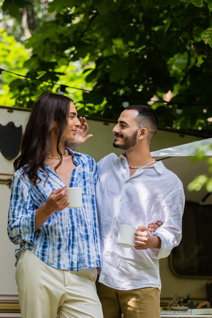 glückliches schwules Paar mit Kaffeebechern, während es sich im Sommer in der Nähe von Lieferwagen anschaut - Foto, Bild