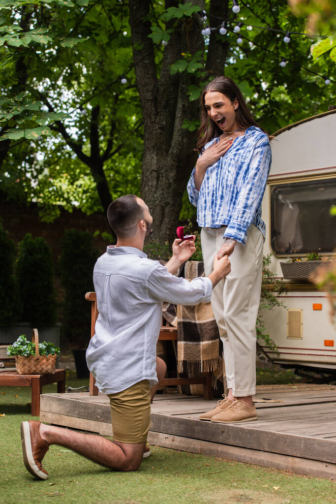gay man making proposal while holding jewelry box with ring near surprised boyfriend during journey in summer  - 写真・画像