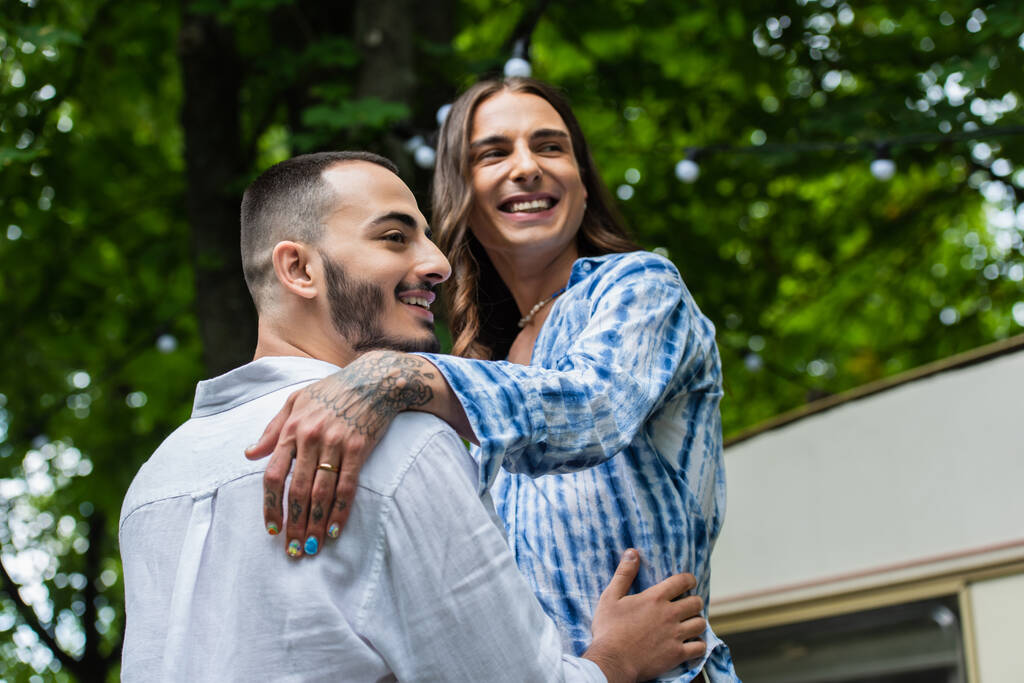 bajo ángulo vista de casado gay pareja sonriendo mientras abrazo cerca van  - Foto, Imagen