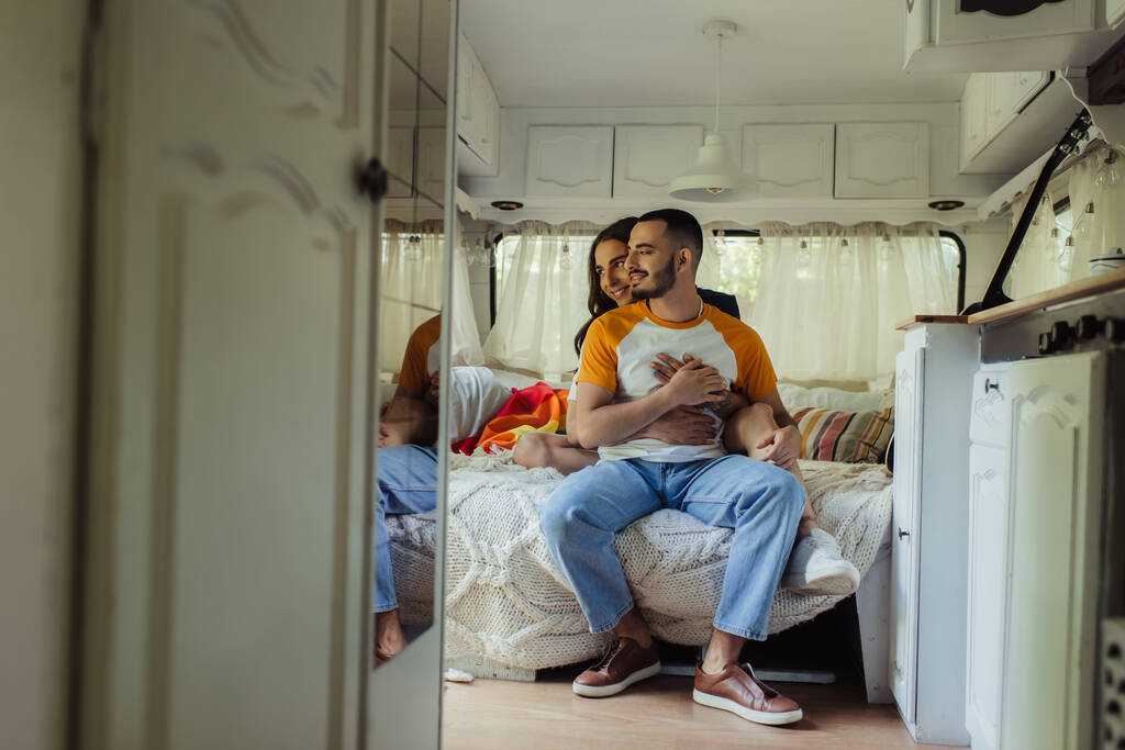 щасливий гей чоловік з довгим волоссям обіймає радісного хлопця на ліжку в сучасному фургоні
  - Фото, зображення