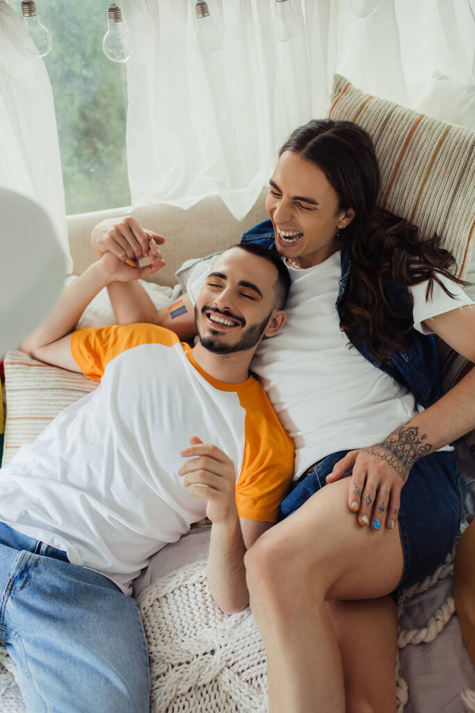 alto angolo vista di sorridente gay uomo con tatuaggi sdraiato sul letto con barbuto fidanzato in moderno van  - Foto, immagini