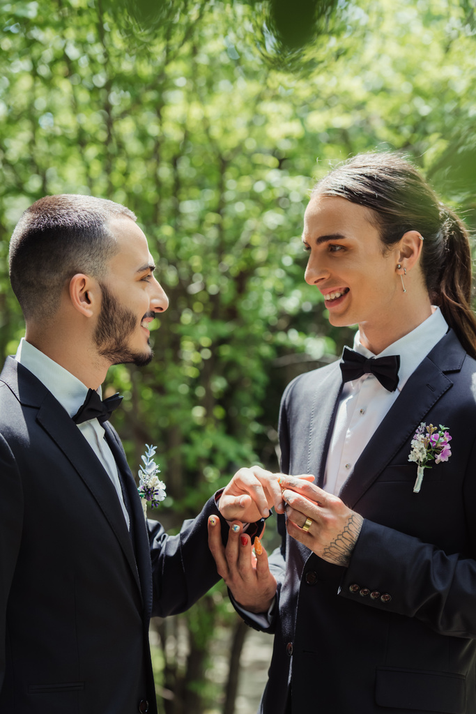 πλαϊνή άποψη του χαρούμενου gay άνδρα φορώντας βέρα στο δάχτυλο του χαρούμενου γαμπρού  - Φωτογραφία, εικόνα
