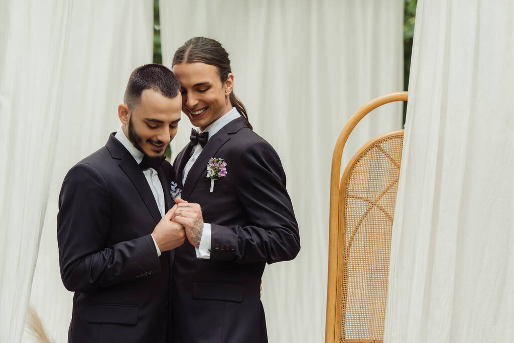 happy gay couple in suits with boutonnieres holding hands on wedding day - Photo, image