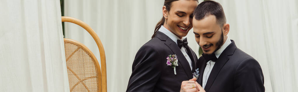 feliz pareja gay en trajes con boutonnieres tomados de la mano en el día de la boda, bandera - Foto, Imagen