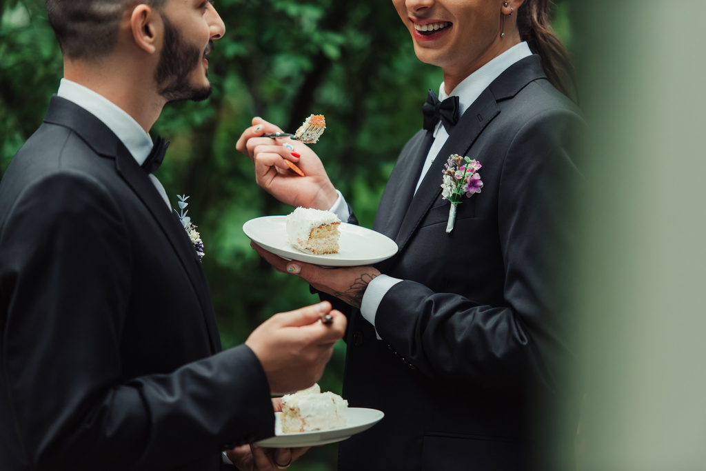 cropped view of happy gay newlyweds in formal wear holding wedding cake  - 写真・画像
