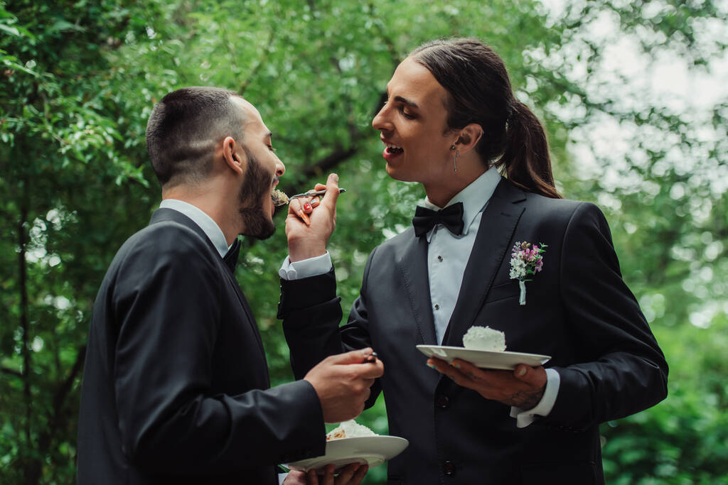tattooed gay man in formal wear feeding husband with wedding cake - Valokuva, kuva