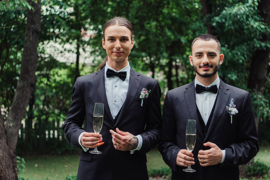 gay νεόνυμφοι με κοστούμια που κρατούν ποτήρια με σαμπάνια την ημέρα του γάμου  - Φωτογραφία, εικόνα