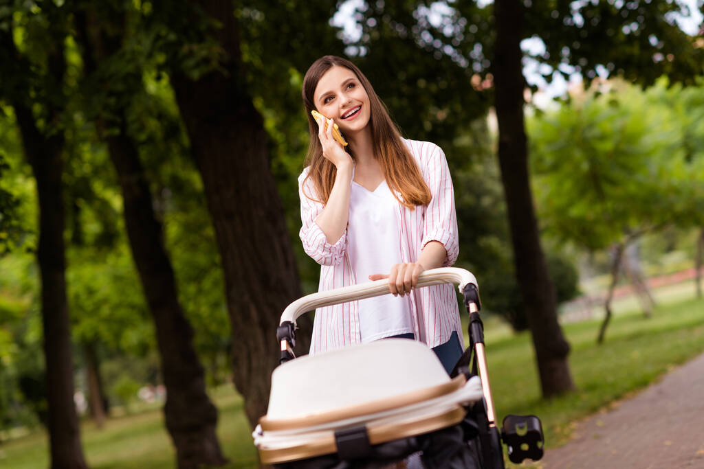 Fénykép álmodozó bájos anya viselni alkalmi ruhát beszél modern szerkentyű élvezze séta kislánya baba kocsi kívül kert. - Fotó, kép