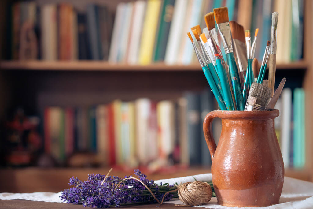 Still life of paint brushes  in clay jug, old books in the background. - Foto, Imagen