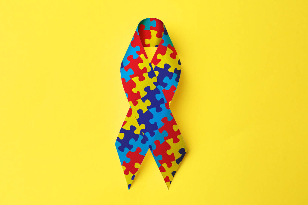 Всесвітній день аутизму. Барвиста стрічка-головоломка на жовтому тлі, вид зверху
 - Фото, зображення