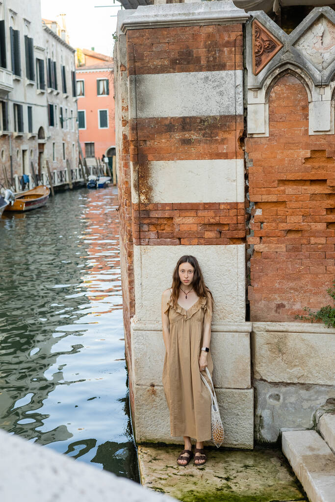 Young woman in dress looking at camera near old building in Venice  - 写真・画像