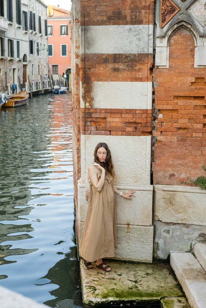 Pregnant woman in dress holding string bag near river and building in Venice  - 写真・画像