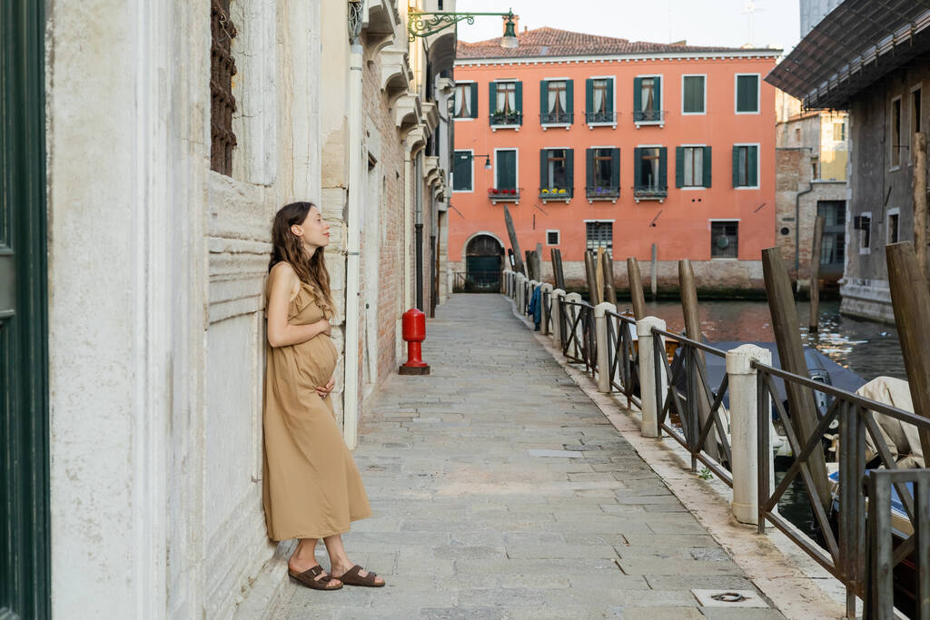 Vista lateral de la mujer embarazada de pie cerca del antiguo edificio en la calle en Venecia  - Foto, Imagen