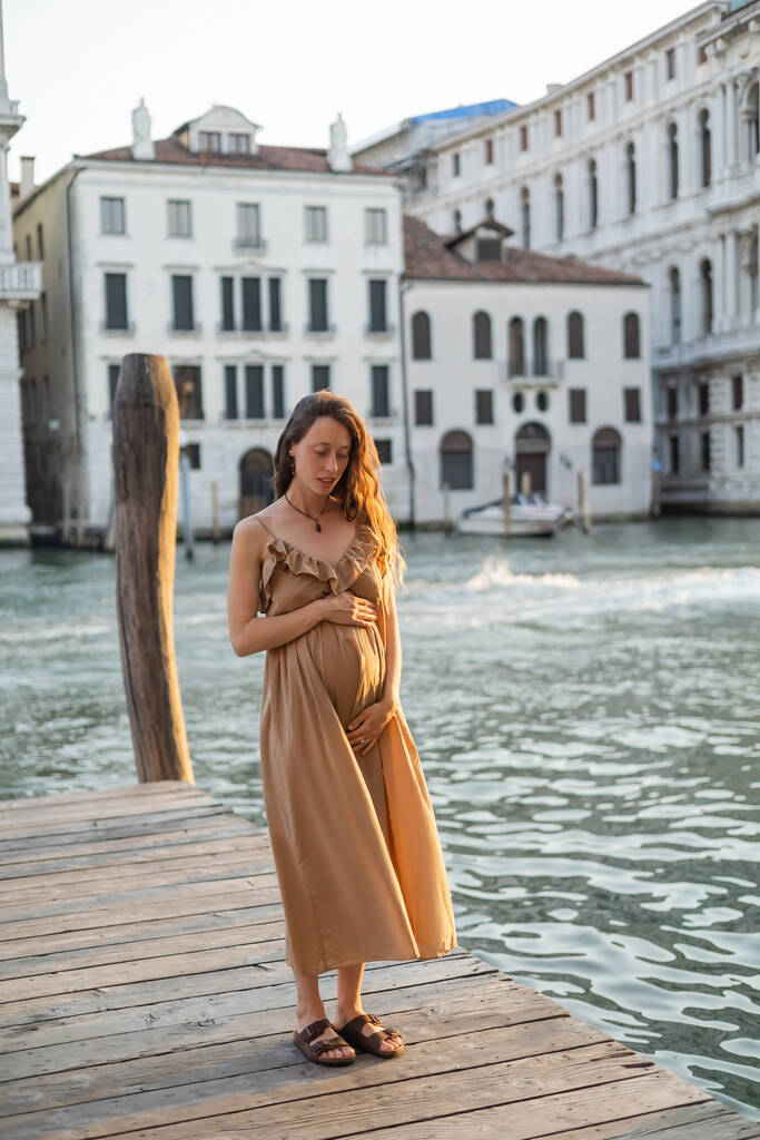 Вагітна жінка в літній сукні стоїть на дерев "яному пірсі у Венеції.  - Фото, зображення