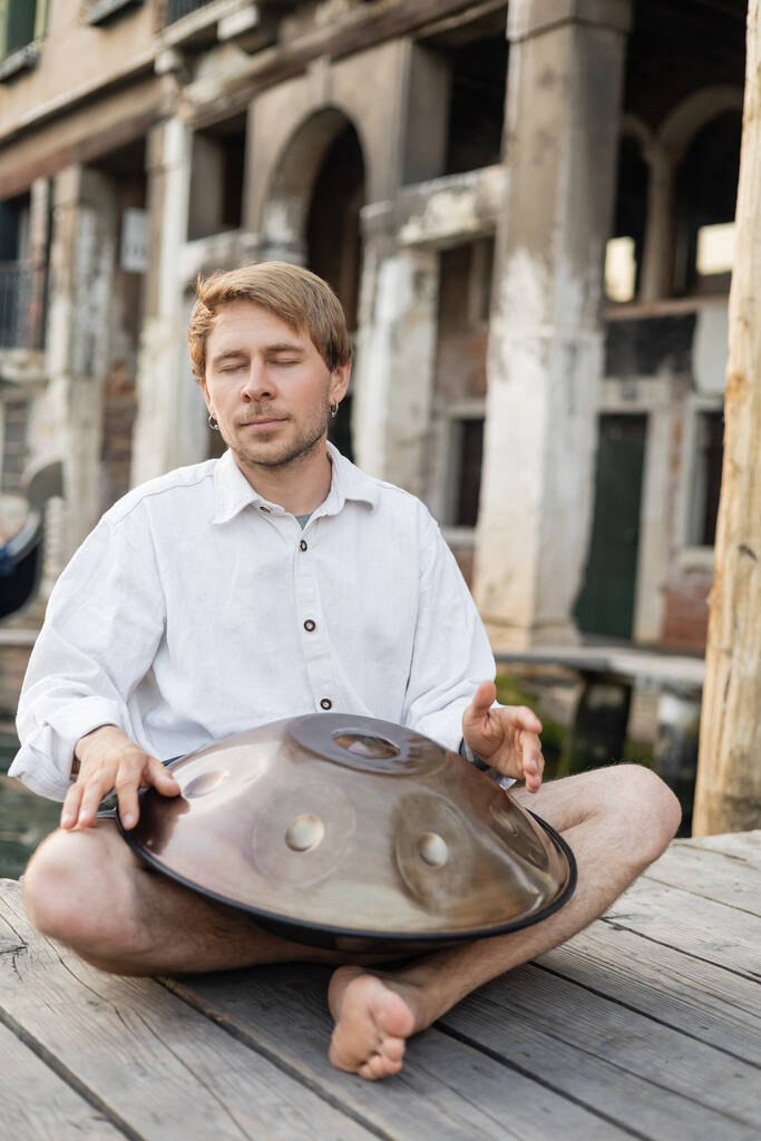 Музыкант с закрытыми глазами играет на барабане на деревянном пирсе в Венеции  - Фото, изображение
