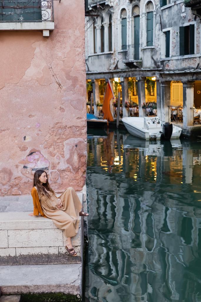 Side view of young pregnant woman sitting on stairs of building in Venice  - 写真・画像
