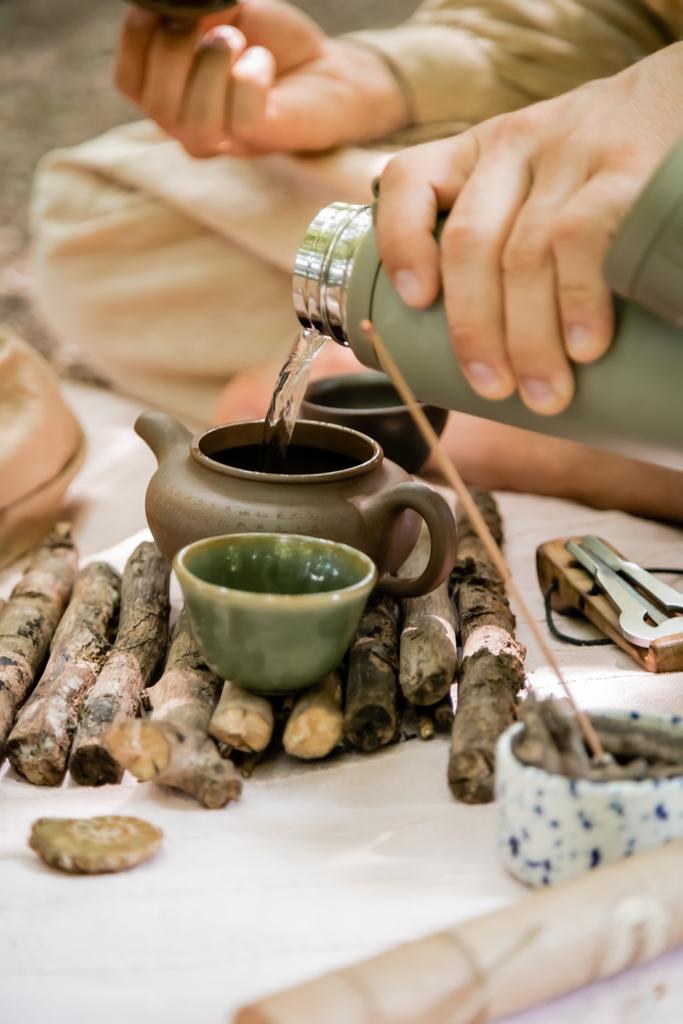 Обрезанный вид человека, заливающего горячую воду в чайник во время чайной церемонии в лесу  - Фото, изображение