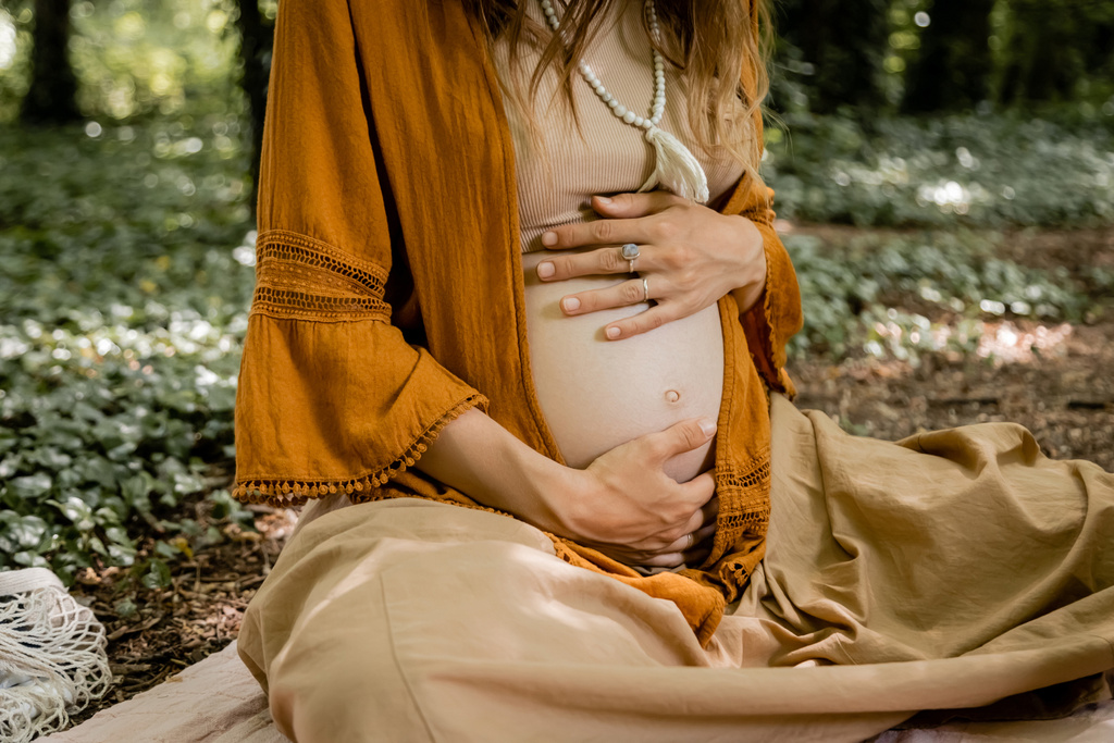 Ausgeschnittene Ansicht einer jungen Schwangeren, die ihren Bauch im Wald berührt  - Foto, Bild
