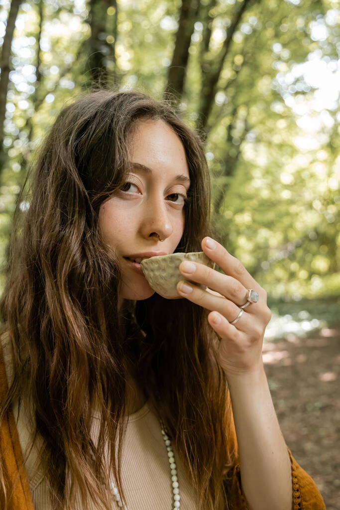 Junge brünette Frau trinkt Tee aus Schüssel im Wald  - Foto, Bild