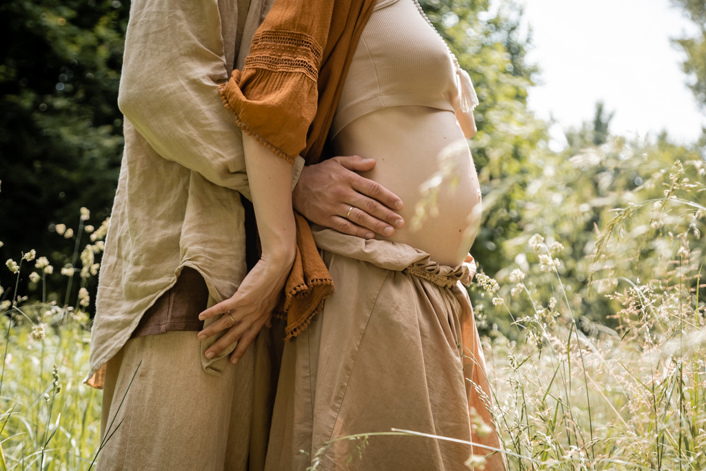Cropped view of man hugging pregnant woman in field  - Photo, Image