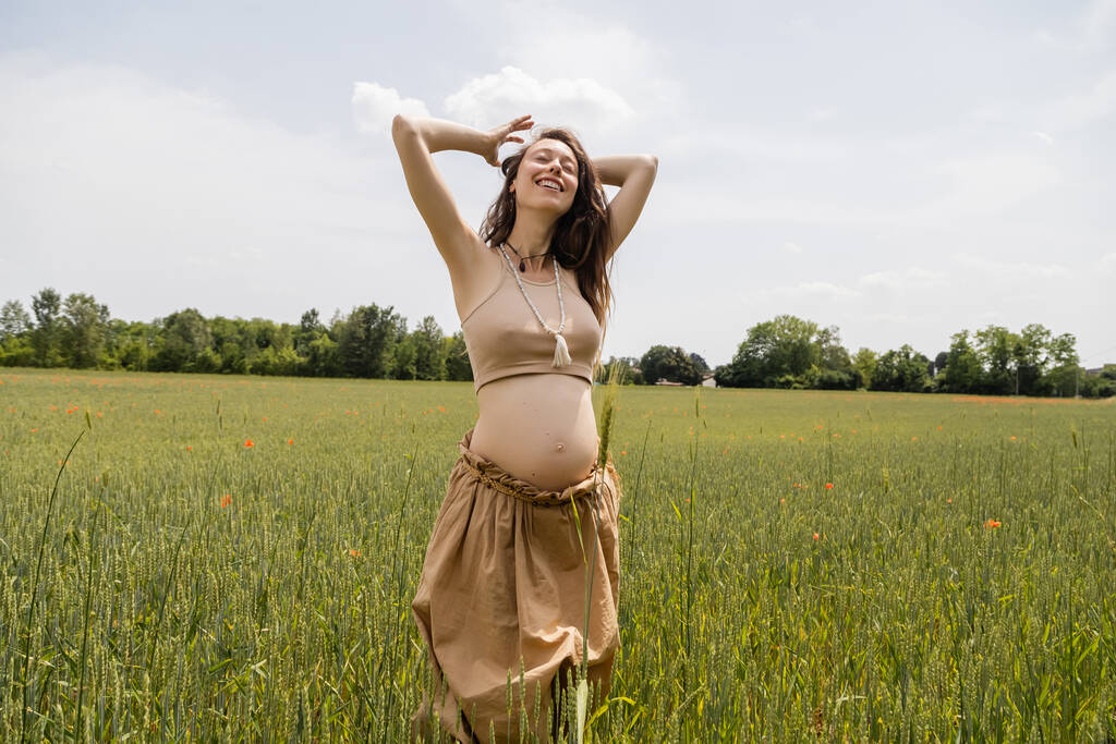 Happy pregnant woman standing in field with spikelets - Foto, Imagem