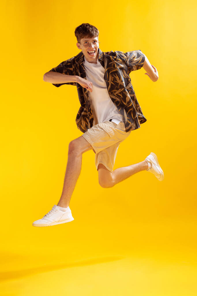Running. Full-length mans portrait isolated on bright yellow studio backgroud. Young emotional man jumping. Human emotions, facial expression concept. Summer fachion collection - Photo, Image