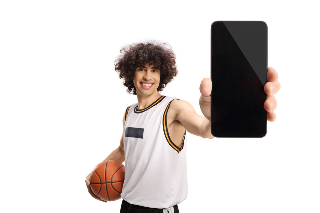 Basketball player holding a ball and showing a smartphone isolated on white background - Fotoğraf, Görsel