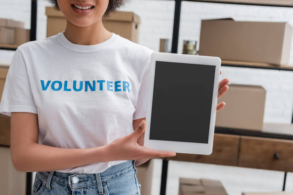 částečný pohled na usmívajícího se afroamerického dobrovolníka držícího digitální tablet s prázdnou obrazovkou v charitativním centru - Fotografie, Obrázek