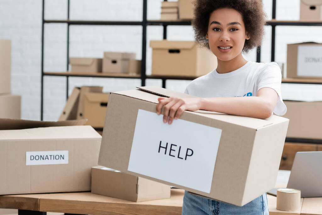 donna afro-americana positiva che tiene la scatola con lettere di aiuto nel centro di volontariato - Foto, immagini