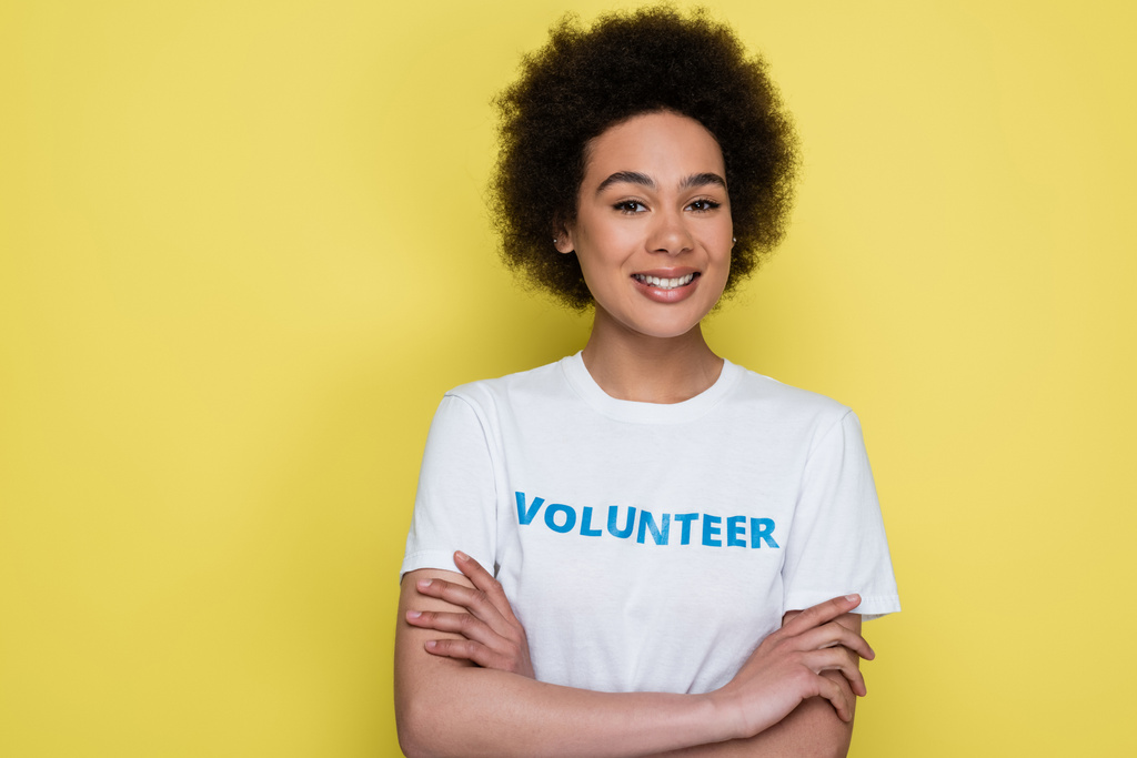 happy african american woman in t-shirt with volunteer lettering isolated on yellow - 写真・画像