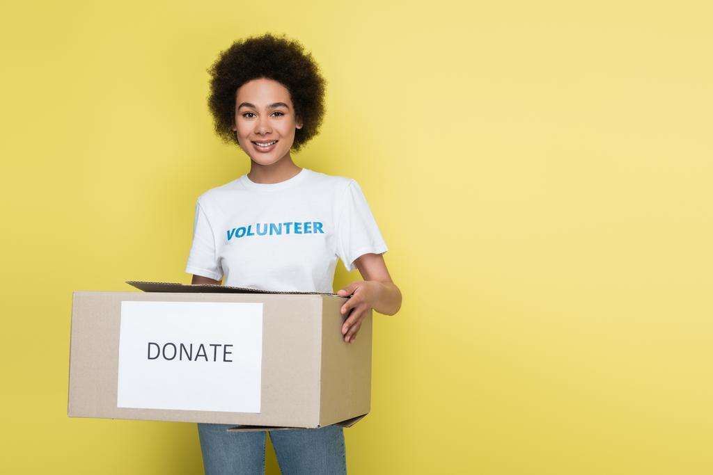 positive african american volunteer holding donate box isolated on yellow - Photo, image