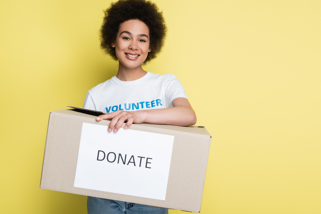 african american volunteer holding charity box with donate lettering isolated on yellow - 写真・画像