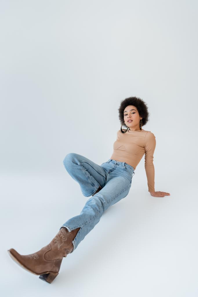 повна довжина афроамериканської жінки в джинсах і сорочці з довгим рукавом на сірому фоні
 - Фото, зображення