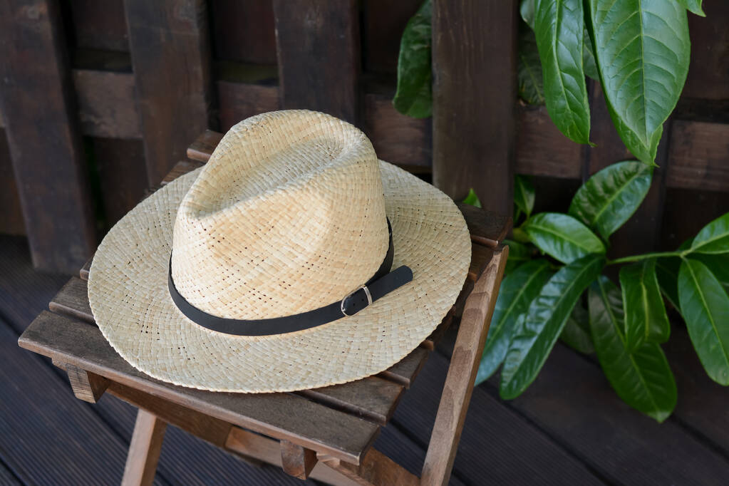 Stylish hat on wooden stool near fence. Beach accessory - 写真・画像