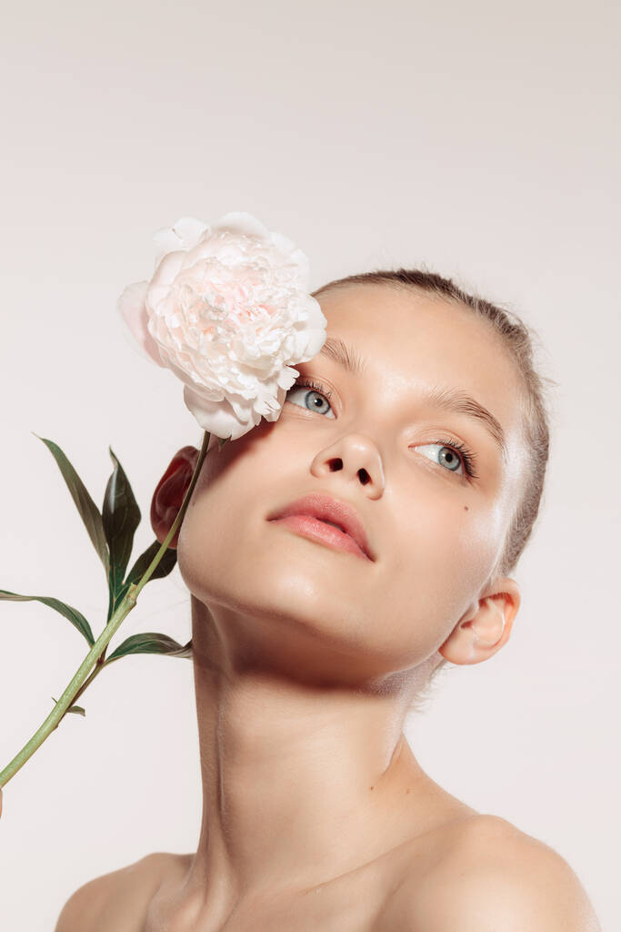 Een pioen. Close-up portret van mooi jong meisje met bloem geïsoleerd over witte studio achtergrond. Naakt kleur, dieet, cosmetica, natuurlijke schoonheid en esthetische cosmetologie concept. Kopieer ruimte voor - Foto, afbeelding