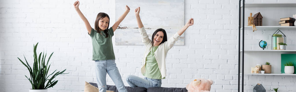 excited woman and girl with outstretched hands in modern living room, banner - Photo, Image