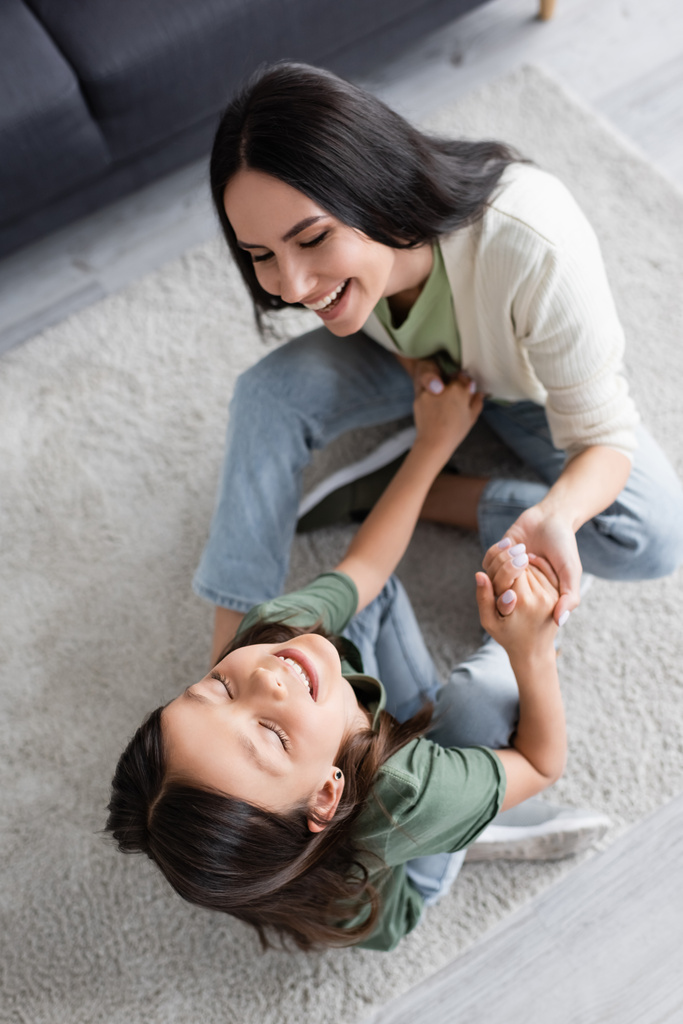top view of cheerful babysitter and girl having fun on carpet at home - Foto, Imagem