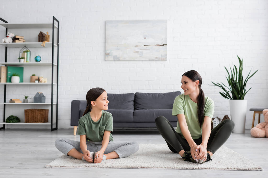 girl and babysitter smiling at each other while sitting on carpet in fire log pose - Foto, Bild
