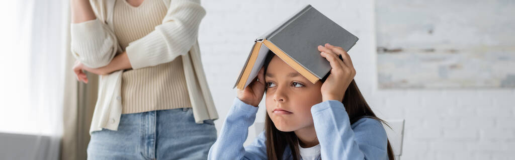bored and tired girl covering head with textbook near babysitter on background, banner - Foto, Bild