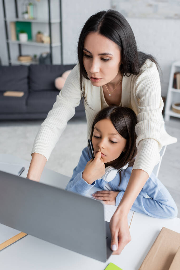 Babysitter schaut während Online-Unterricht auf Laptop neben nachdenklichem Mädchen - Foto, Bild