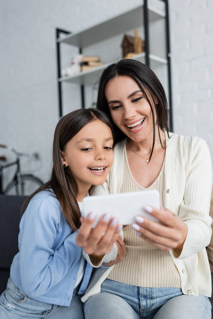 dziecko i niania uśmiechnięte w pobliżu rozmytego smartfona podczas rozmowy wideo w domu - Zdjęcie, obraz