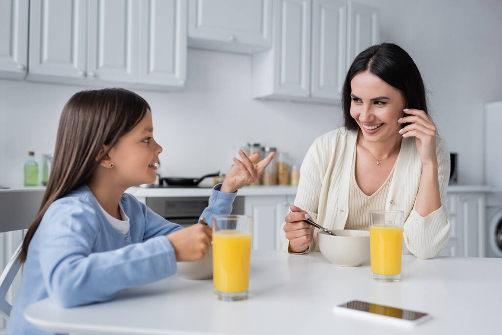 girl talking to happy nanny near bowls with breakfast and fresh orange juice - Zdjęcie, obraz