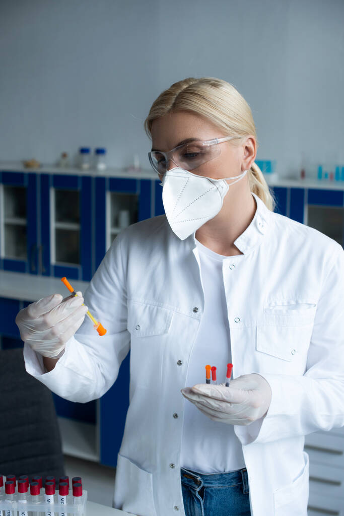 Scientist in protective goggles holding syringes near test tubes in lab  - Foto, Bild
