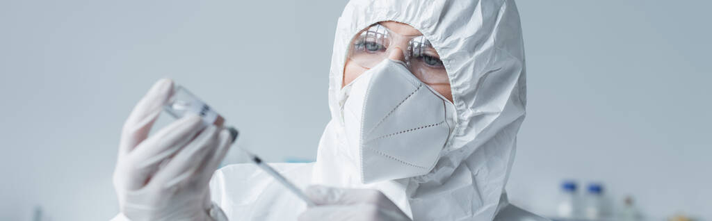 Scientist in protective suit and mask holding syringe and vaccine in lab, banner  - Valokuva, kuva