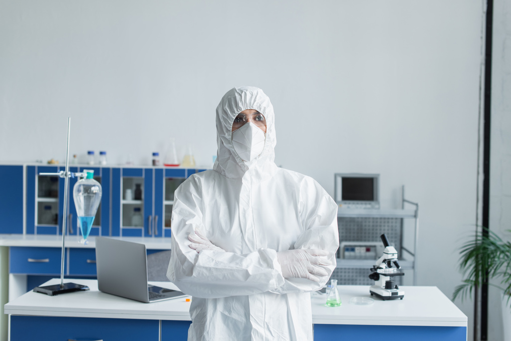 Scientist in hazmat suit and protective goggles crossing arms in lab  - Foto, afbeelding