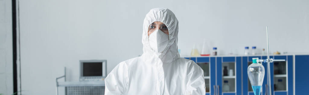 Naukowiec w kombinezonie ochronnym i masce stojącej w laboratorium, transparent  - Zdjęcie, obraz
