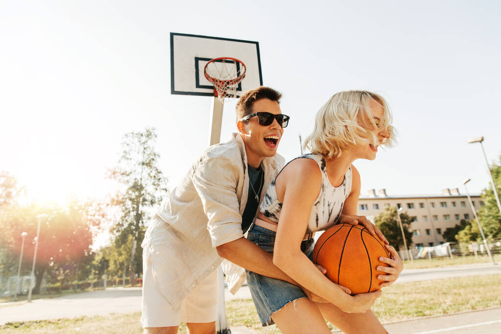 zomervakantie, sport en mensen concept - gelukkig jong paar met bal spelen op basketbal speeltuin - Foto, afbeelding