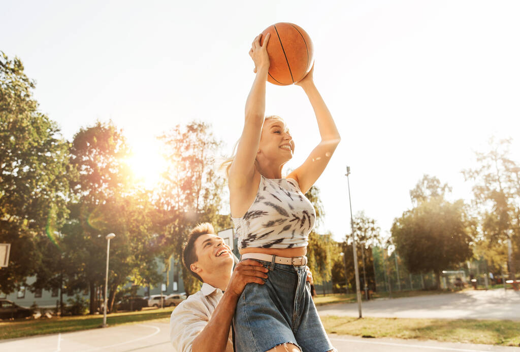 letnie wakacje, sport i koncepcja ludzi - szczęśliwa młoda para z piłką grająca na boisku do koszykówki - Zdjęcie, obraz
