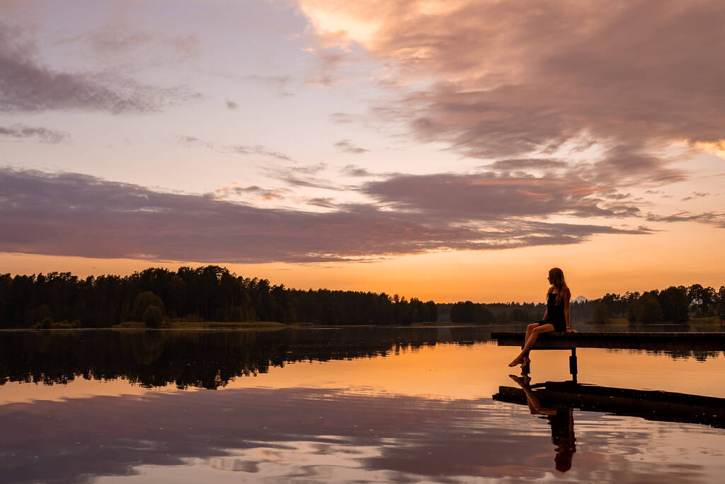 Silhouette solitario ragazza al tramonto sul lago. Donna da sogno che si gode il tramonto arancione vicino al lago in un molo. Ragazza godendo della natura magica. - Foto, immagini