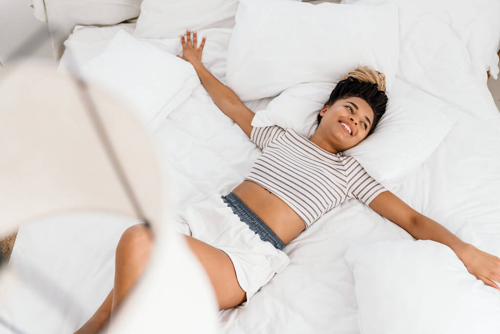 Young black woman laughing while making fun on bed at home - Photo, Image